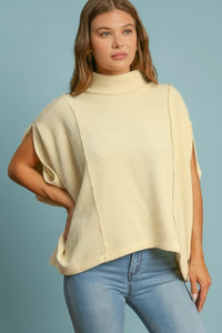 Woman wearing a cream poncho and blue jeans against a brown background