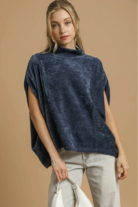 Woman wearing a navy blue poncho over a beige outfit on a beige background