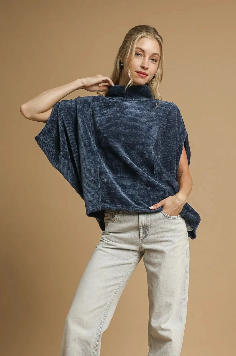 Woman wearing a navy blue turtleneck sweater and light gray jeans on a brown background