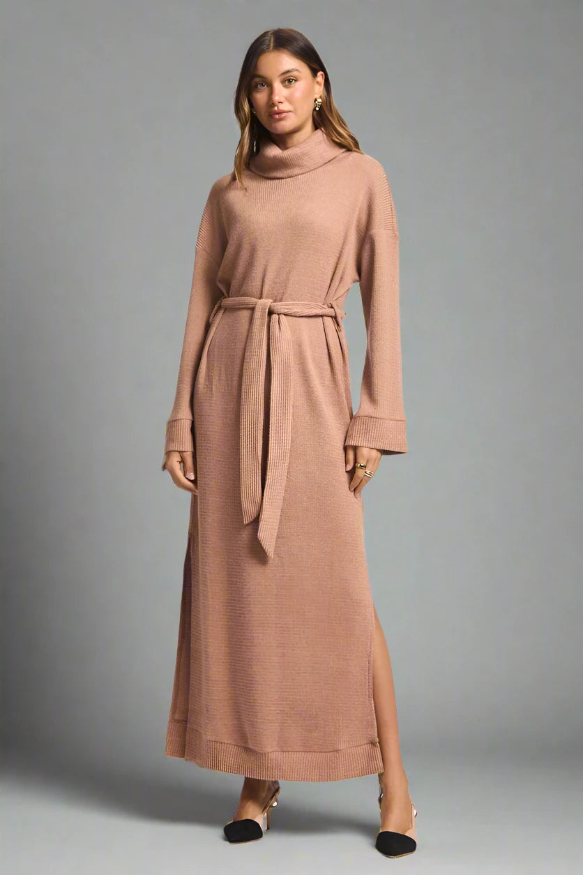 Woman wearing a long brown dress with a belt on a plain background.