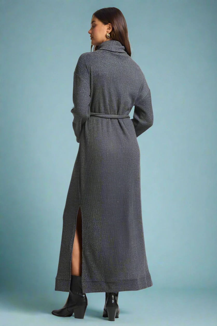 Woman wearing a long gray dress with a belt on a plain background.