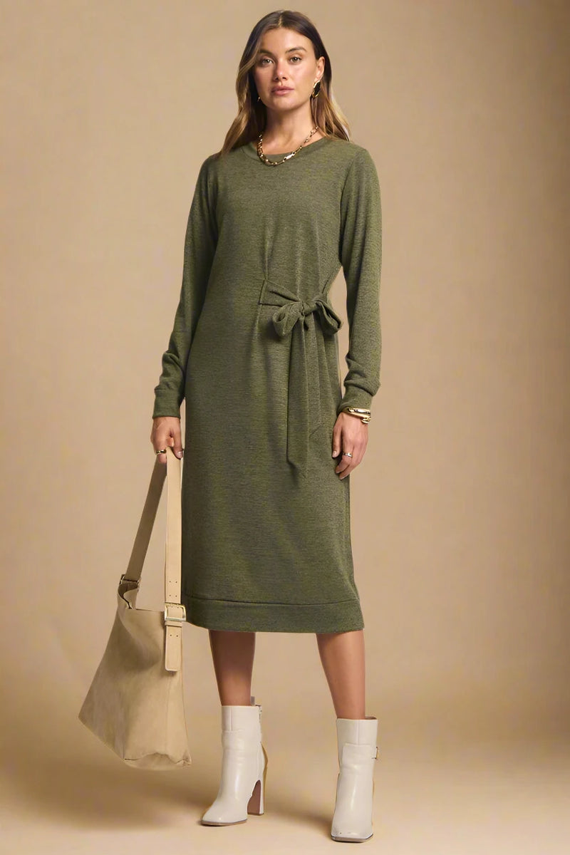 Woman wearing a green dress with a beige bag and boots on a plain background