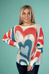 Model is wearing a light knit sweater with dolman sleeves and a teal and red heart pattern.