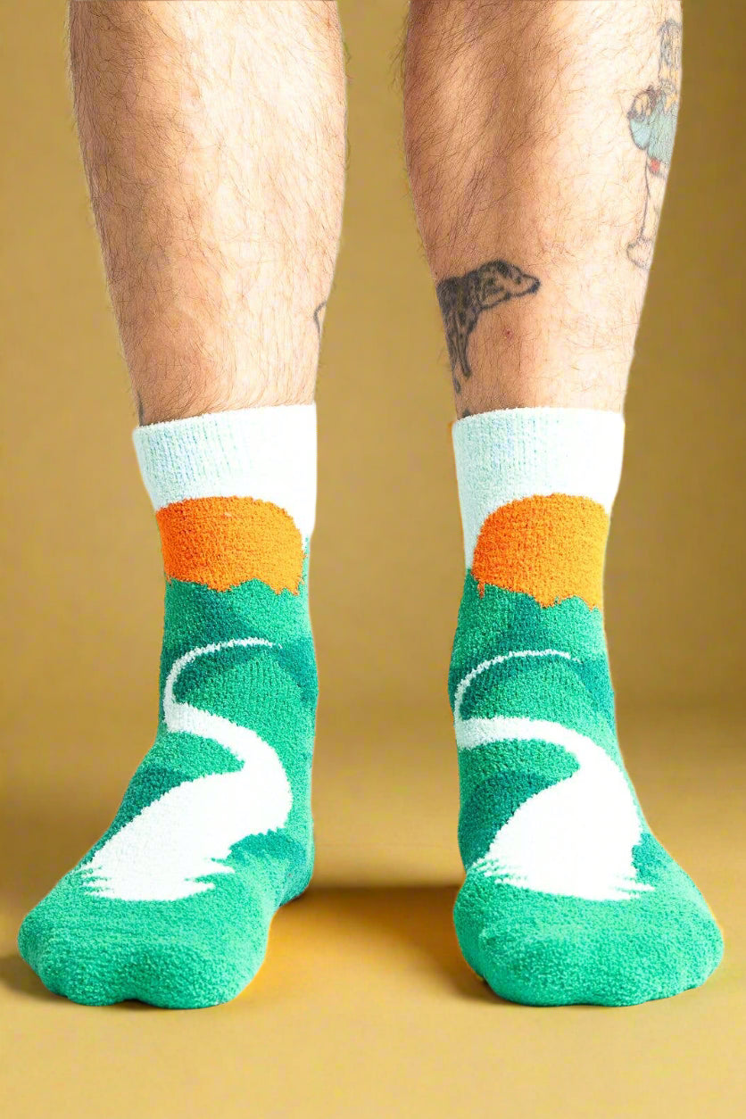 Green socks with white swan design and orange accents worn by a person on a white background