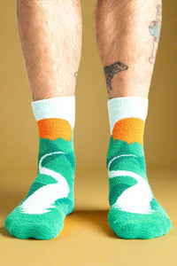 Green socks with white swan design and orange accents worn by a person on a white background