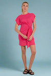 Woman wearing a bright pink dress with a knot detail on a plain background