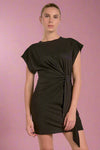 Woman wearing a black dress with a knot detail on a plain background