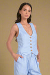 Woman wearing a light blue vest over a matching outfit on a plain background