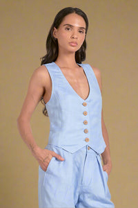 Woman wearing a light blue vest over a matching outfit on a plain background