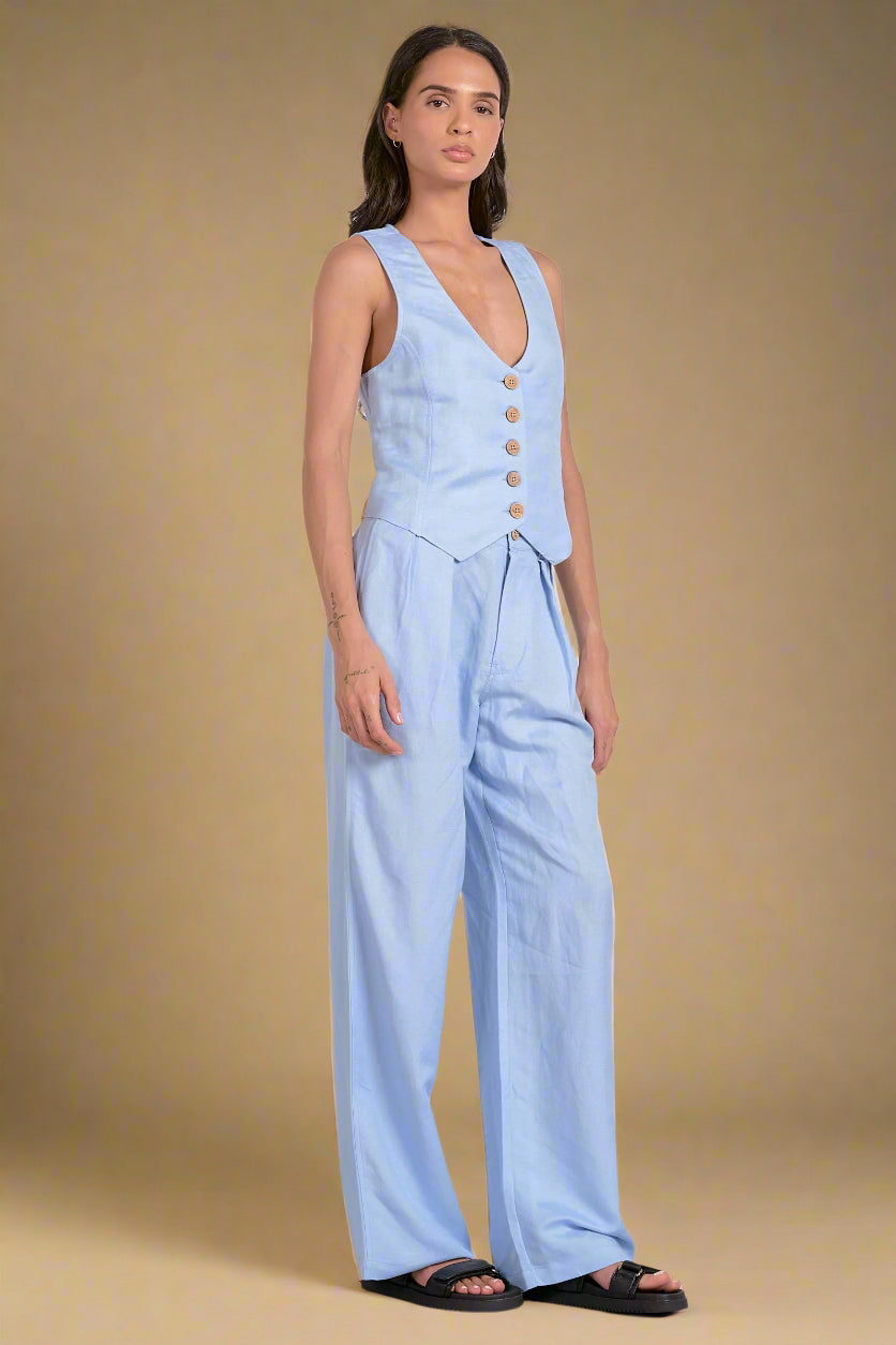 Woman wearing a light blue sleeveless top and wide-leg pants on a white background