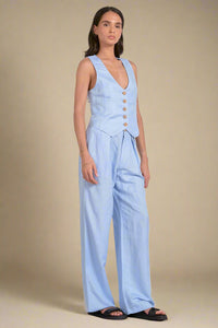 Woman wearing a light blue sleeveless top and wide-leg pants on a white background