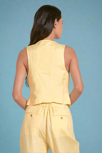 Woman wearing a yellow sleeveless top and pants on a plain background