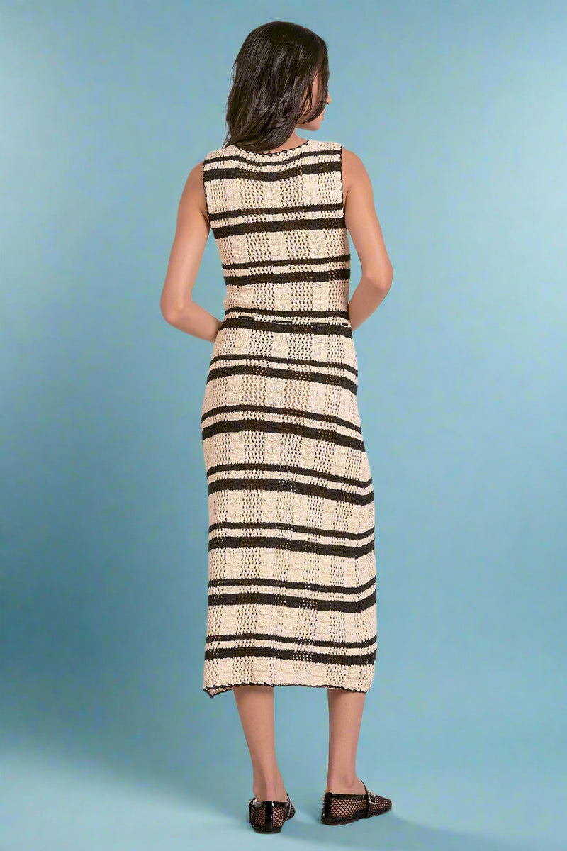 Woman wearing a sleeveless knit dress with black and white striped pattern on a plain background
