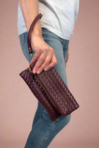 Model is holding a quilted fold-over wristlet clutch with zipper closure. 