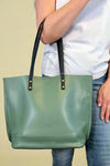 Model is carrying a large color block tote bag with external zippers in olive sage green. 