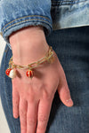 Model is wearing a gold paperclip chain bracelet with red and white charms. 