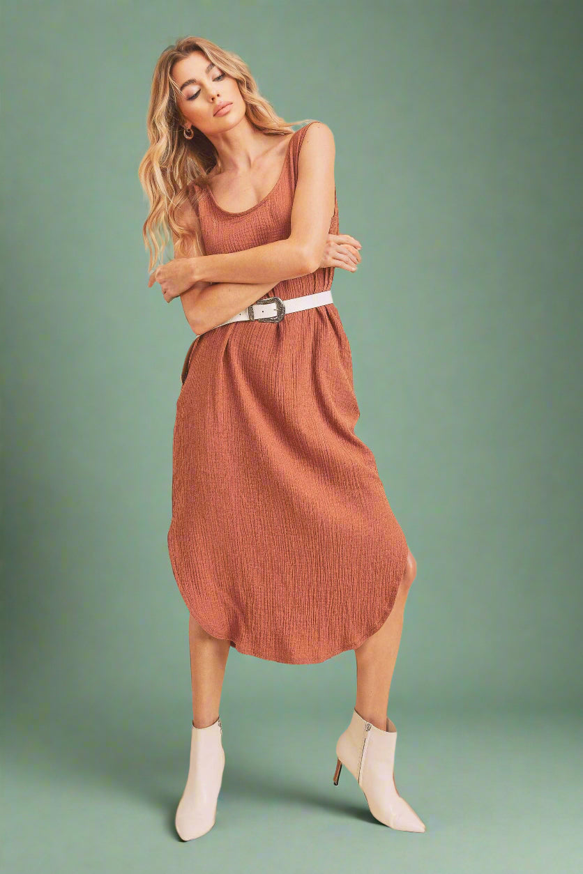 Woman wearing a rust-colored dress with a white belt and white boots on a beige background