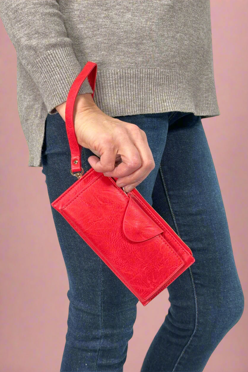 Model is holding a red colored wallet that doubles as a wristlet. 