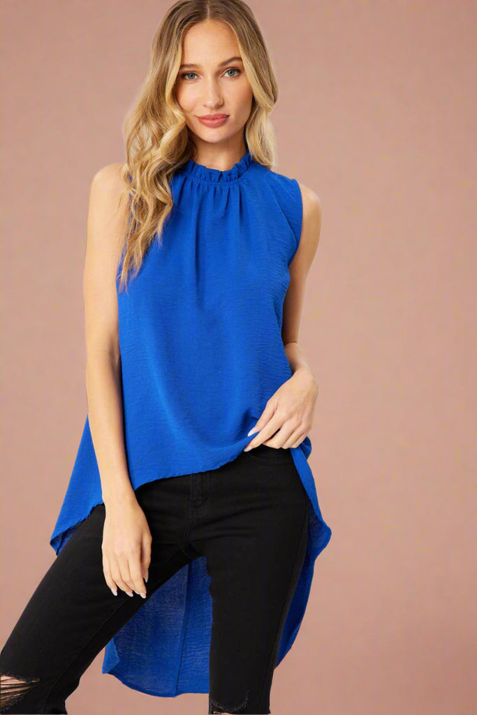 Model is wearing a bright royal blue top. It has a ruffle on the neck line and a high low cut. 