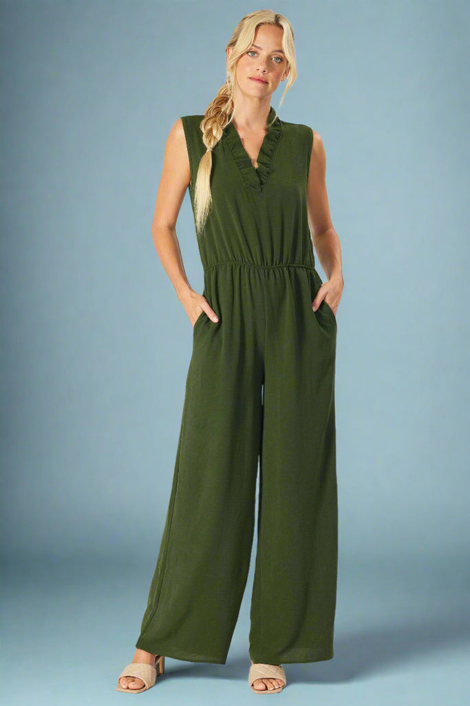 Model is wearing a flattering olive jump suit with a ruffled v neck, elastic waistband and pockets. 