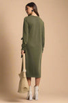 Woman wearing a green dress holding a beige bag on a plain background
