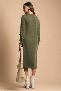 Woman wearing a green dress holding a beige bag on a plain background