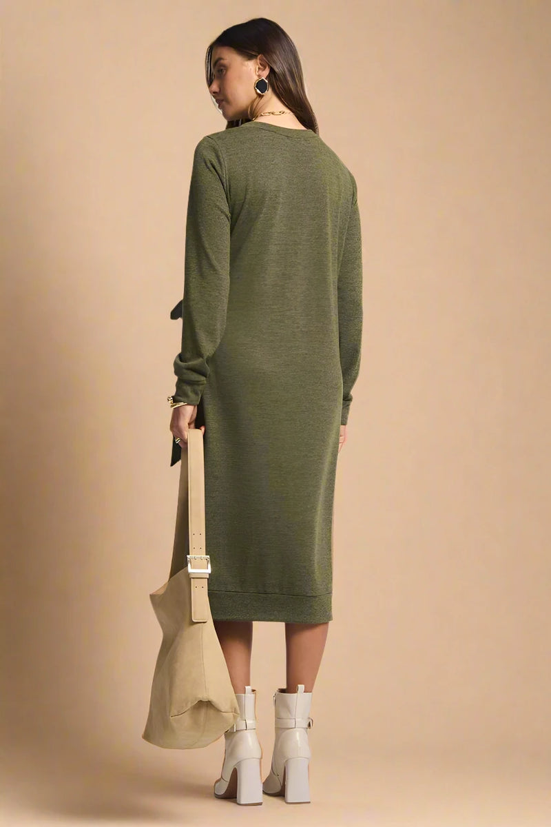 Woman wearing a green dress holding a beige bag on a plain background