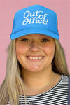 A light blue adjustable trucker hat with the phrase ‘Out of Office!’ on the front.