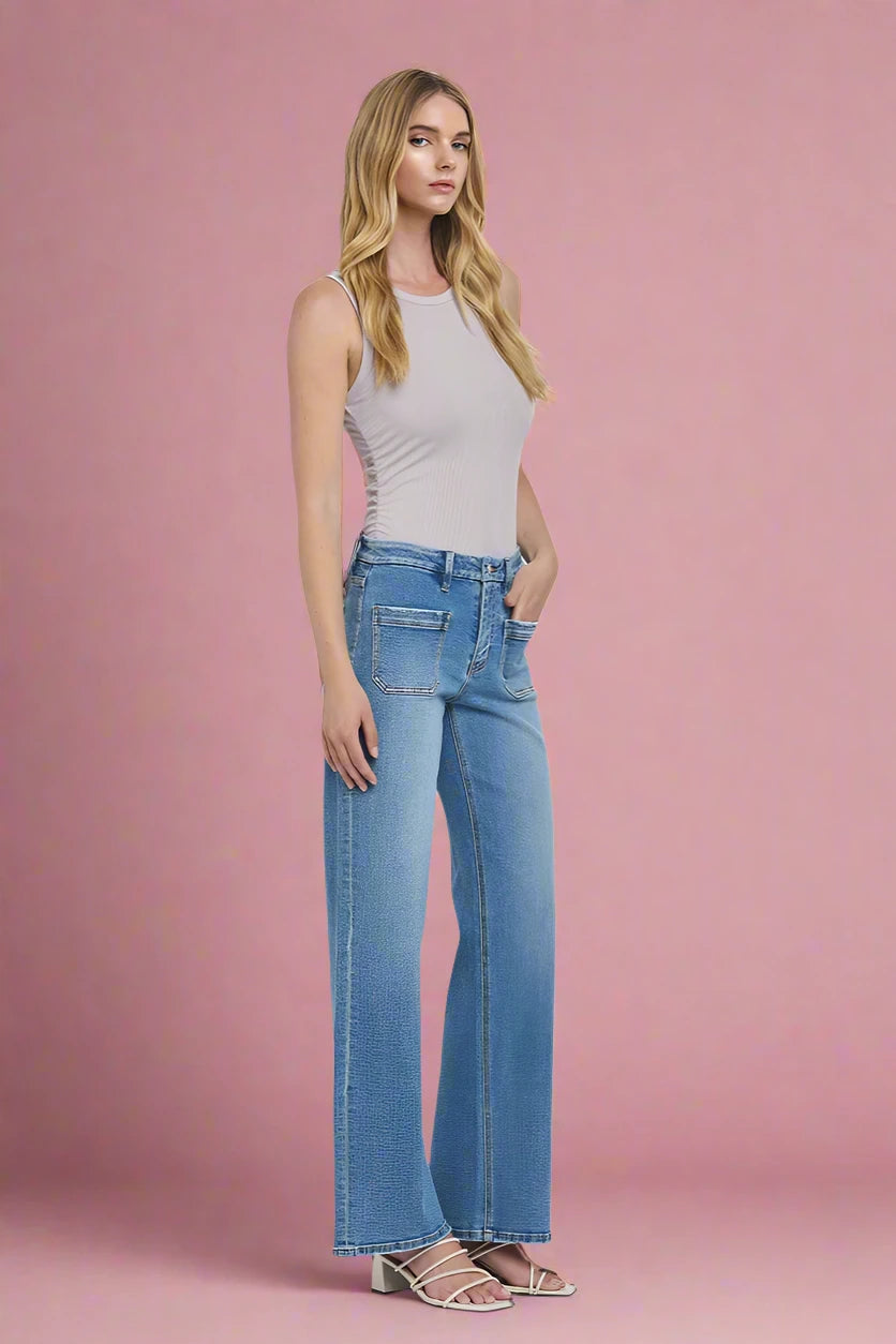 Woman wearing blue jeans and a light gray tank top against a plain background.