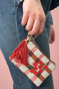 Model is carrying a small beaded coin purse with cherries and red tassel. 