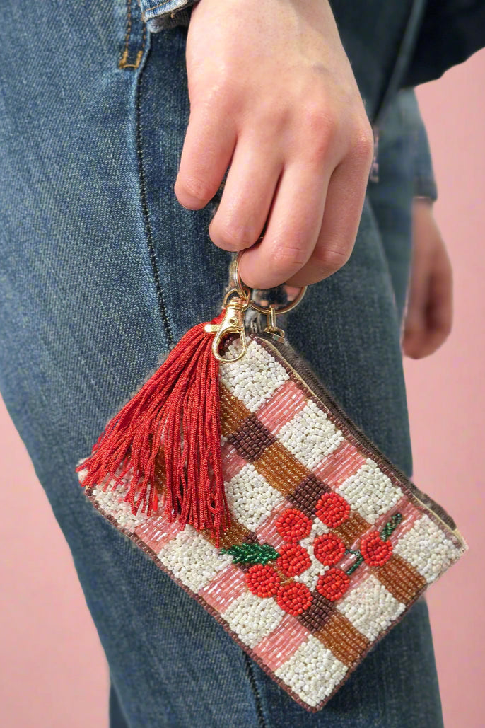 Model is carrying a small beaded coin purse with cherries and red tassel. 