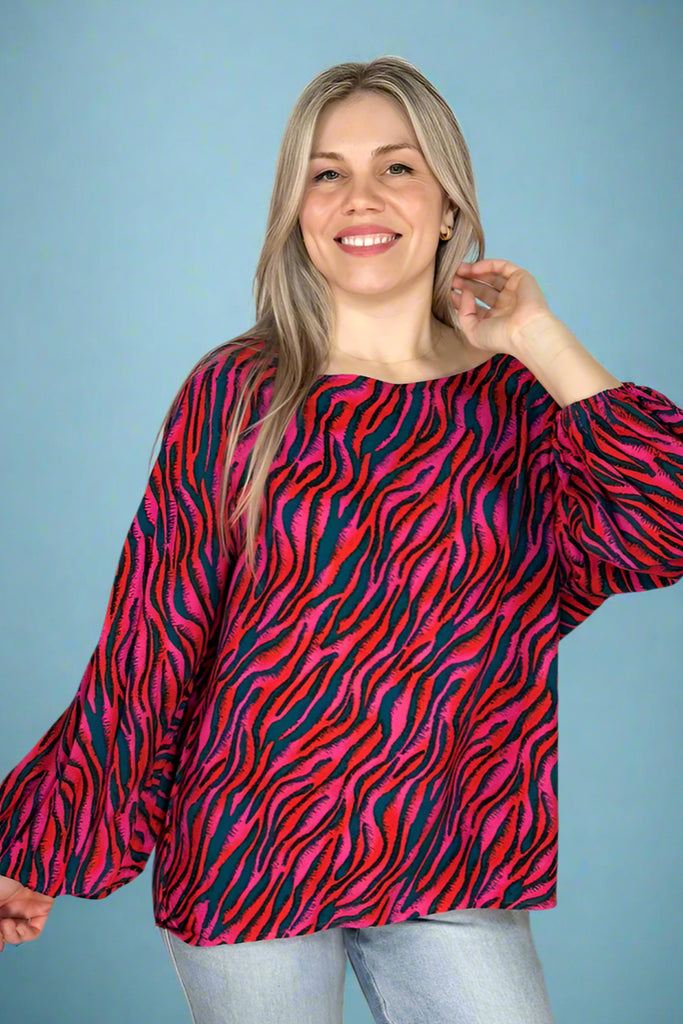 A women’s oversized lightweight blouse featuring vibrant zebra print in pink, red, and teal, boat neckline, and lantern sleeves.