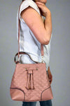 Model is carrying a rosewood colored, quilted bucket bag. Bag has a handle, crossbody strap and removable wristlet. 