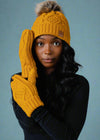 Woman wearing a mustard yellow knit hat and gloves against a gray background