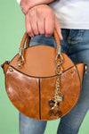 Model is carrying a small circle purse with braided handle, gold keychain and exterior pockets. Includes a cross body strap. 