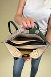 Model is carrying a large color block tote bag with external zippers in olive sage green. 