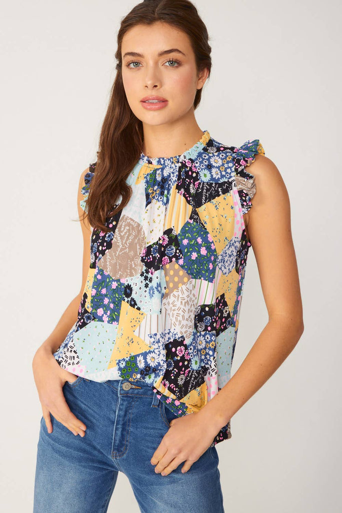 Model is wearing a cute patchwork top with ruffle neck and arm details. The top is sleeveless with a long line. Features a mix of patterns primarily navy and floral. 