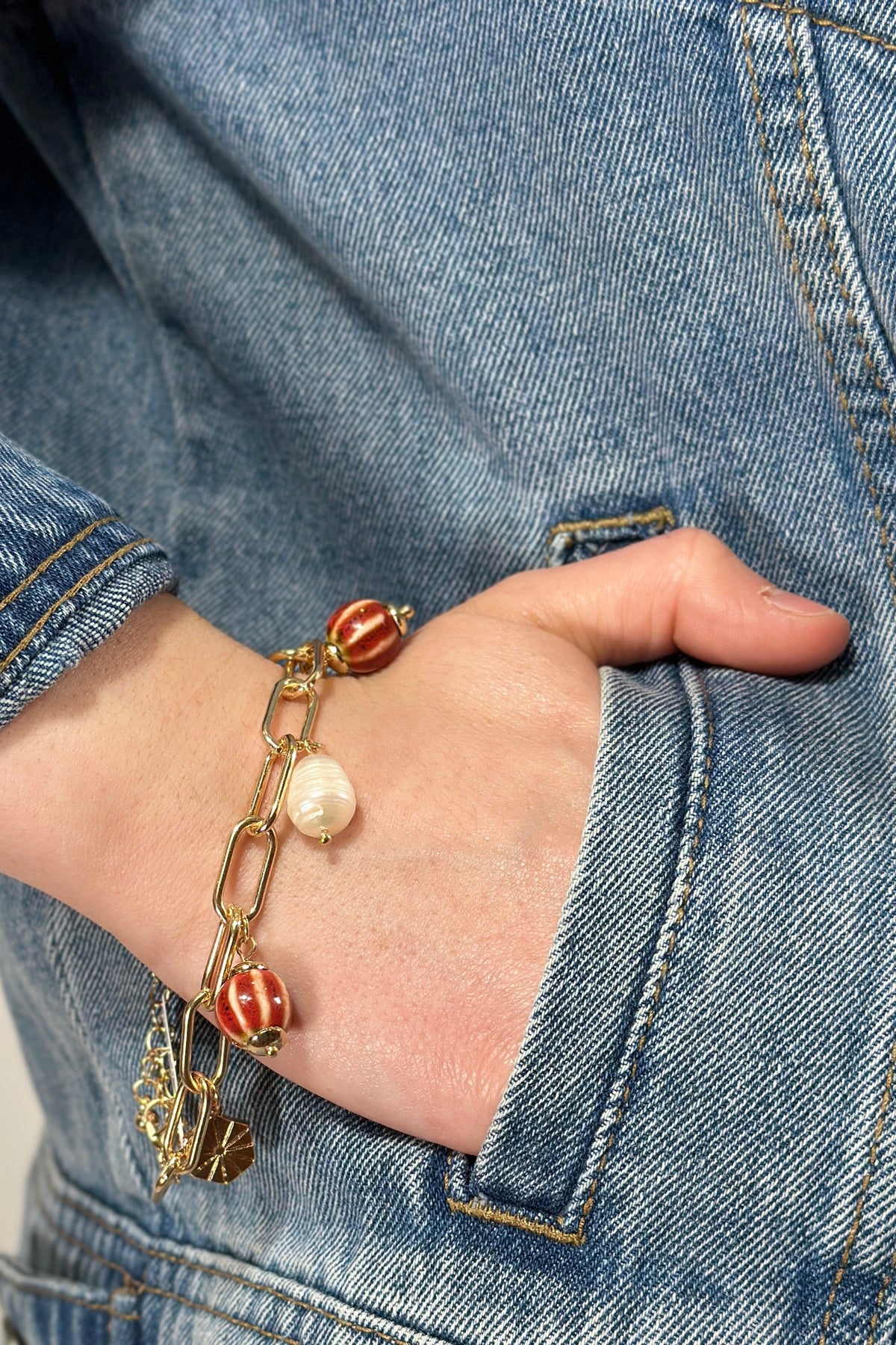 Model is wearing a gold paperclip chain bracelet with red and white charms. 