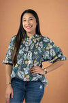 Woman wearing a floral blouse with rolled-up sleeves against a plain background