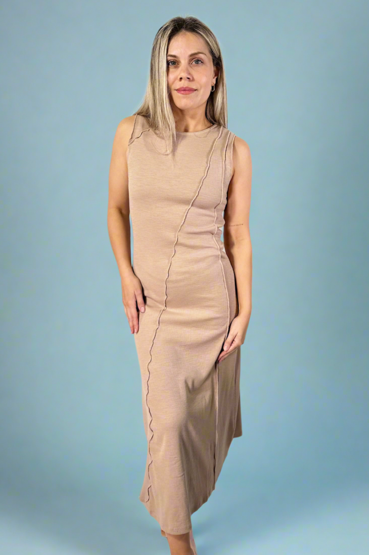 Model is wearing a taupe colored sleeveless maxi dress with exposed seam detailing. 