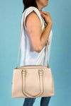Model is wearing a large natural colored satchel with multiple compartments. 