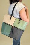 Model is carrying a large color block tote bag with external zippers in olive sage green. 