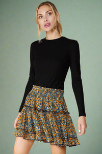 Model is wearing a floral mini skirt featuring an elastic waistband. The skirt is navy blue with an all over floral print in mustard yellow. It is fully lined and has ruffled details. 