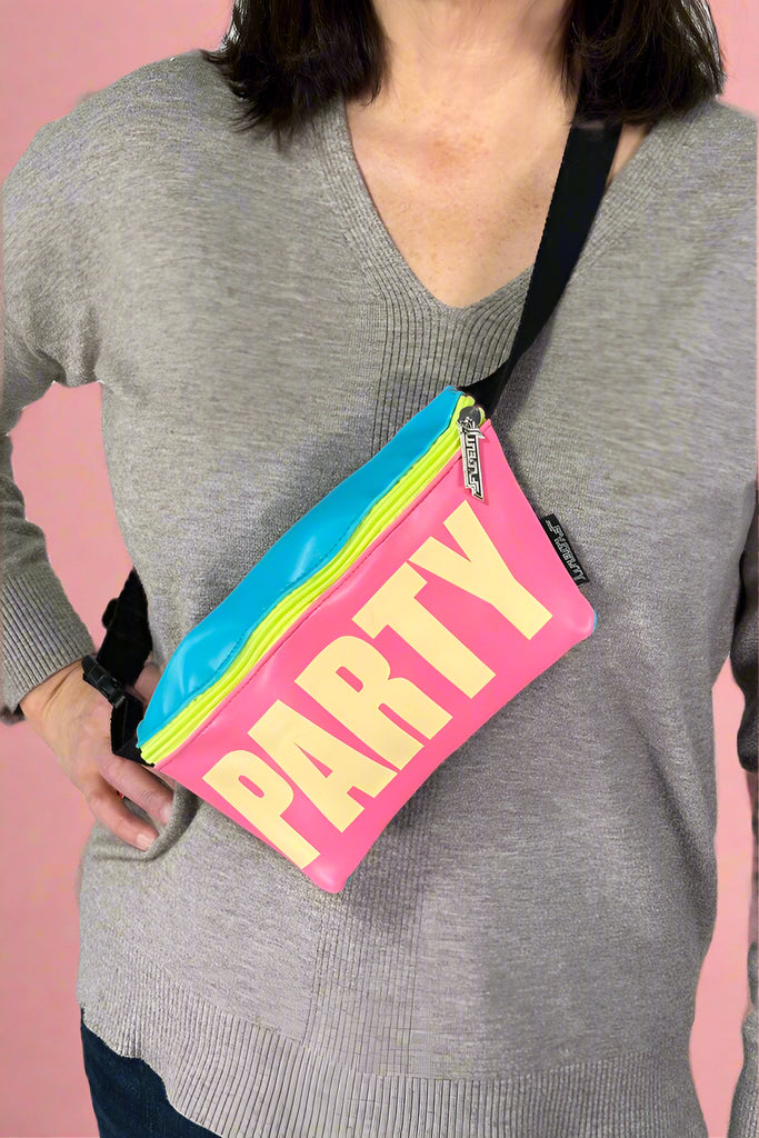 Model is wearing a retro neon color blocked fanny pack bag with an adjustable canvas strap and "PARTY" printed across the front in bold glow in the dark lettering. 