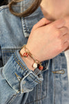 Model is wearing a gold paperclip chain bracelet with red and white charms. 