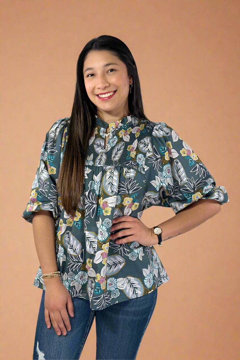 Woman wearing a floral blouse and jeans against a plain background