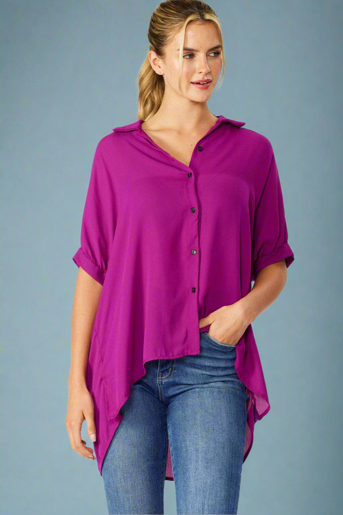 Model is wearing an oversized button down shirt in magenta featuring short dolman sleeves. 