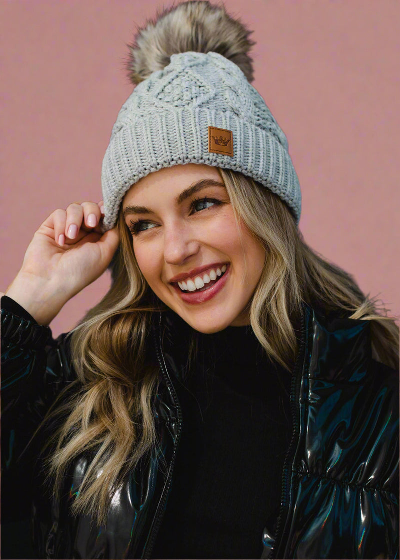 Woman wearing a gray knit beanie with a pom-pom against a black background
