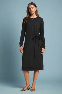 Woman wearing a black dress with a tie waist on a plain background