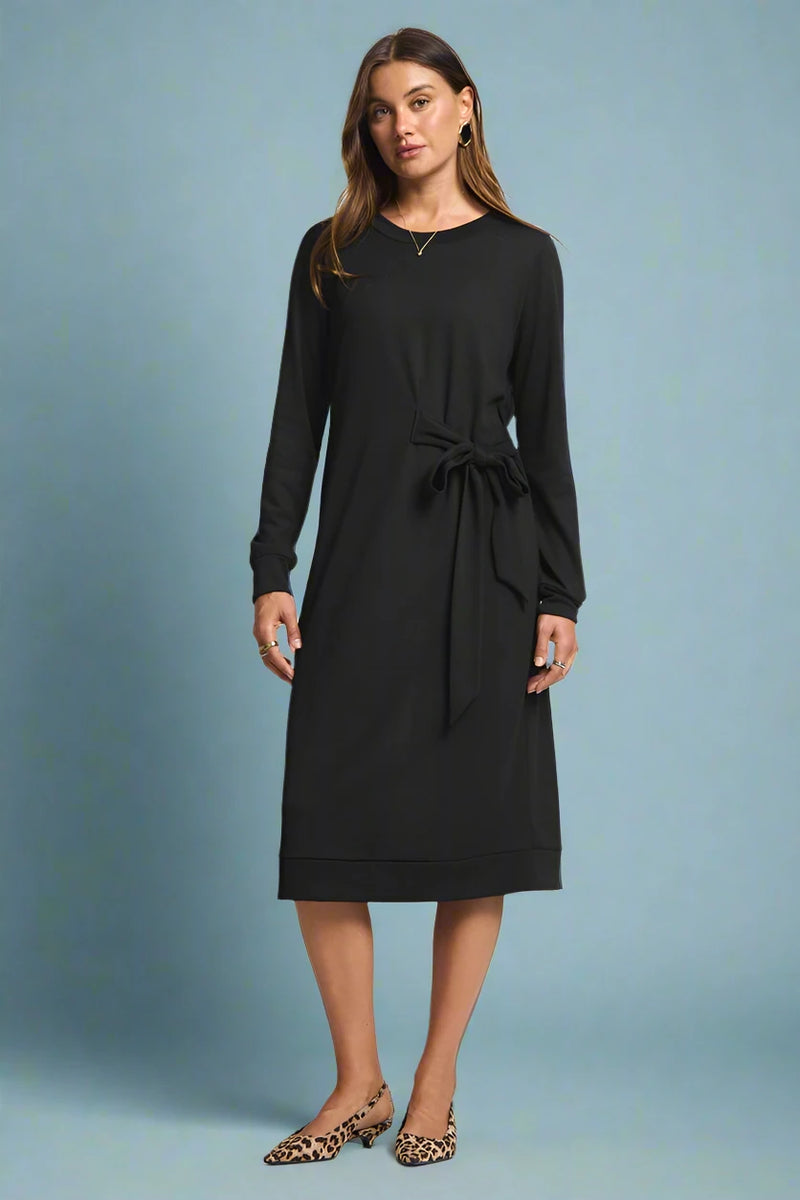 Woman wearing a black dress with a tie waist on a plain background